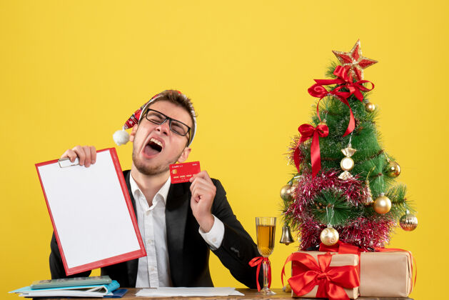 圣诞正面图：男工人拿着银行卡和钞票围着圣诞树 在黄色的树上打哈欠人围着小