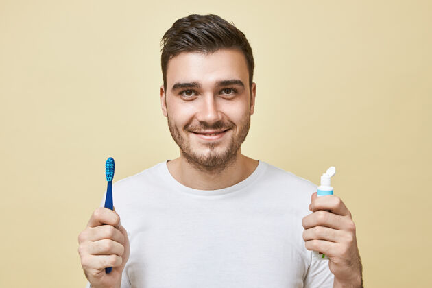 男人一个自信开朗的黑发年轻人的孤立形象 他拿着刷子和牙膏管 一醒来就刷牙卫生 晨练和牙齿美白概念表情成人牙膏