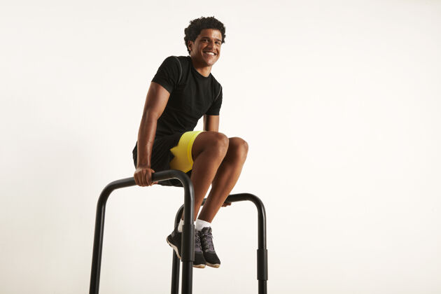 体重快乐微笑的非洲裔美国人 穿着黑色合成运动服 在家里做双杠运动 在白色场地上与世隔绝健美健美教练