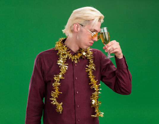 年轻遗憾的是 年轻的金发男子戴着一副戴着金箔花环的眼镜 戴着一杯香槟 低头望着绿色的背景触摸低垂男人