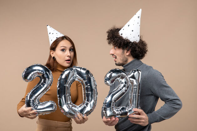 男人表情混乱的快乐年轻夫妇戴新年帽为摄像女孩摆姿势表情情侣肖像