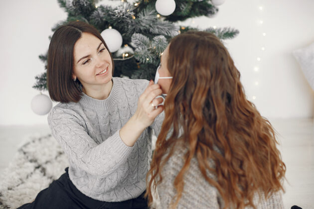 家庭冠状病毒和圣诞节的概念女人帮她的朋友戴口罩面具年房子