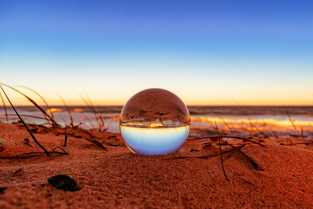 海洋海滩上一个水晶球的特写镜头 周围的环境反射在上面橙色球体彩色