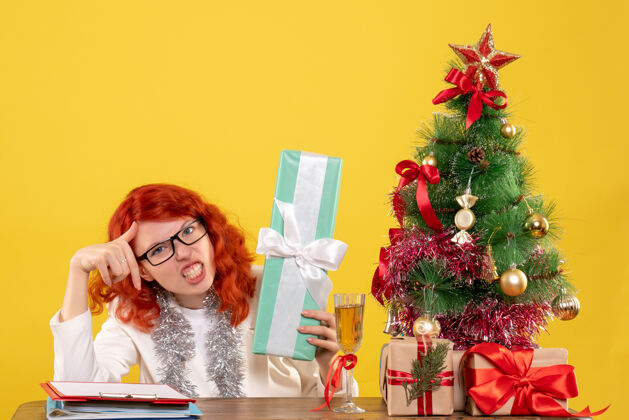 插花前视图：女医生拿着圣诞礼物和黄色背景上的圣诞树坐着新郎树礼物