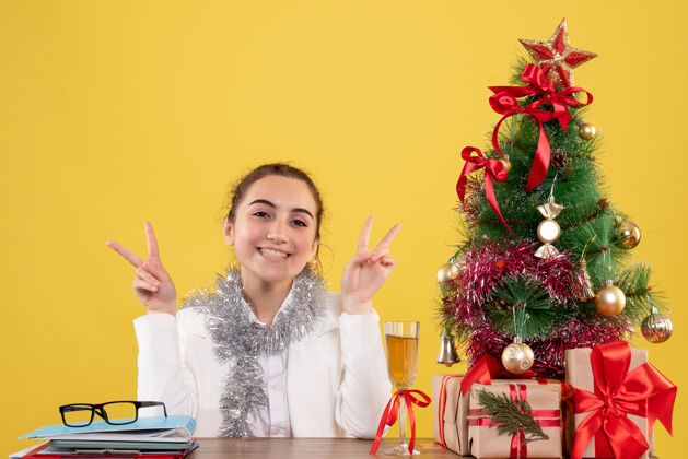 花正面图：女医生坐在黄色背景的桌子后面 还有圣诞树和礼品盒圣诞节前面人