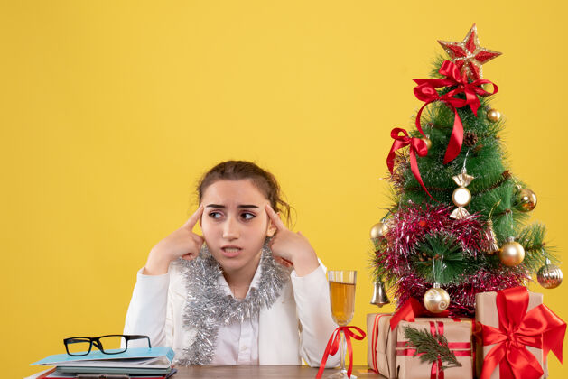 花正面图：女医生坐在黄色背景的桌子后面 还有圣诞树和礼品盒背景快乐前面