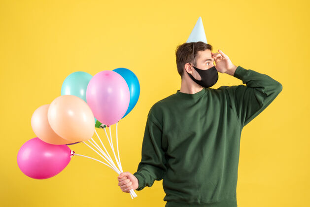 人正面图：戴着派对帽和彩色气球的年轻人在看黄色的东西男人乐趣幸福