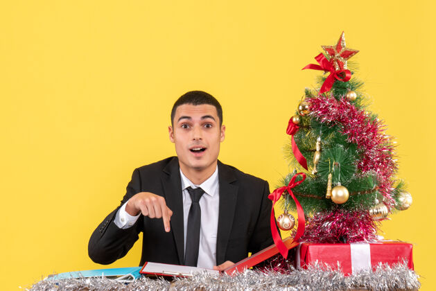 穿西装的男人正面图西装革履的男人坐在桌子旁用手指着文件圣诞树和礼物商人礼物坐着