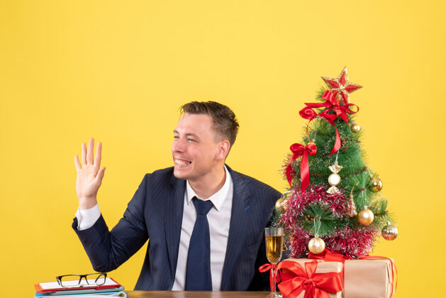新郎帅哥招呼某人坐在圣诞树旁的桌子前 黄色的礼物黄色帅哥礼物