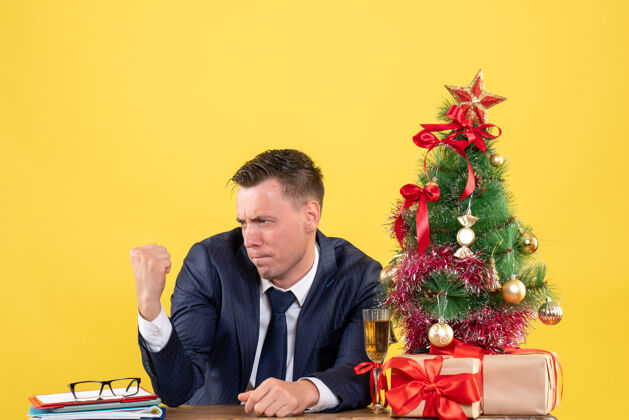 男人西装革履的男人正看着自己坐在圣诞树旁的桌子上 黄色的礼物行政人员公司圣诞节