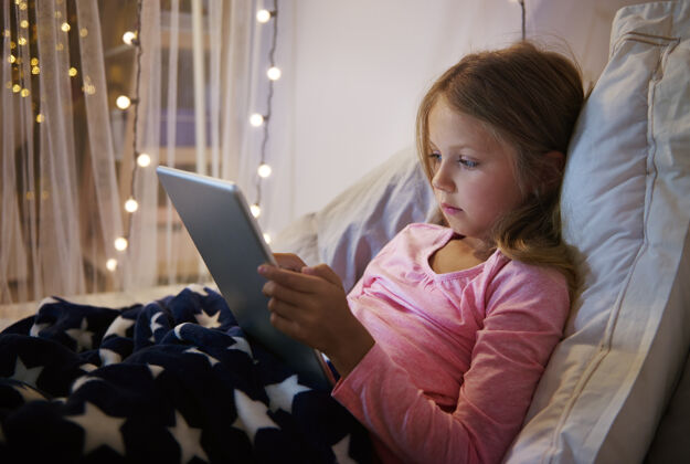 睡觉时间躺在床上使用数码平板电脑的女孩照明背部触摸板