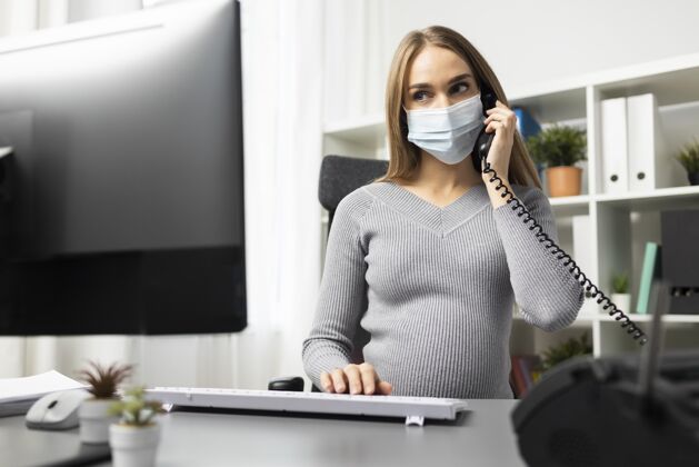 职业孕妇戴着医用口罩在办公桌上打电话女性职业母亲