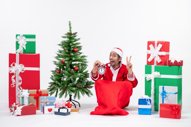 庆祝圣诞老人伸出两个手指 拿着礼物盒和圣诞树坐着树展示快乐