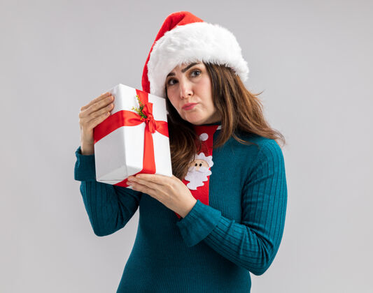 圣诞节失望的成年白人妇女 戴着圣诞帽 打着圣诞领带 拿着圣诞礼盒 白色背景 有复制空间成人失望圣诞老人