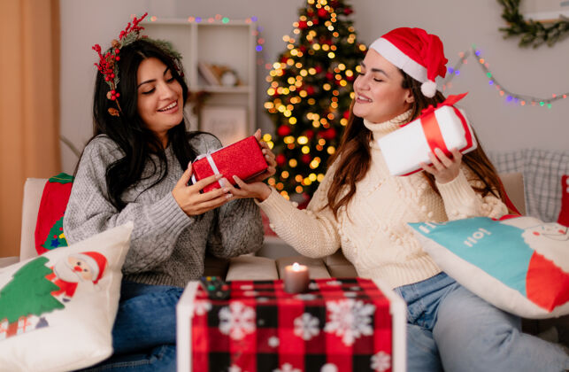 冬青可爱的年轻女孩戴着圣诞帽 戴着冬青花环 看着摆在扶手椅上的礼品盒 在家里享受圣诞时光快乐年轻时间