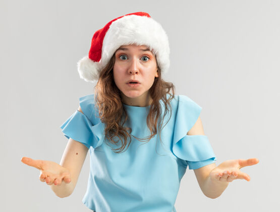 圣诞戴着蓝色上衣和圣诞帽的年轻女子看起来很困惑 非常焦虑 愤怒和不高兴地举手新的蓝色年