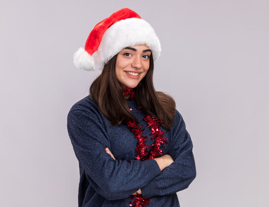 新微笑着的年轻白人女孩戴着圣诞帽 脖子上戴着花环 双臂交叉站着微笑快乐复制