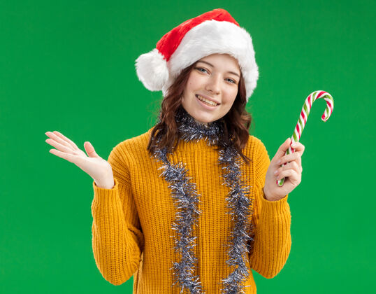微笑戴着圣诞帽 脖子上戴着花环 面带微笑的斯拉夫女孩手持糖果手杖 手一直张开脖子女孩花环