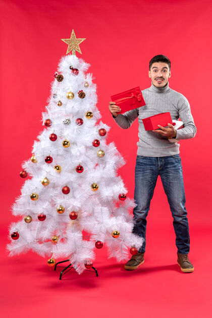 衬衫一个穿着灰色上衣的快乐英俊的成年人站在装饰过的白色圣诞树旁的俯视图礼物上衣圣诞树