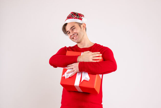 漂亮正面图微笑的年轻人 戴着圣诞帽 手里拿着白色的礼物紧帽子圣诞老人