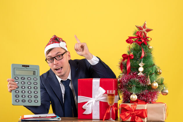 人手持计算器圣诞树和黄色礼物的商务人士的前视图举行人办公室