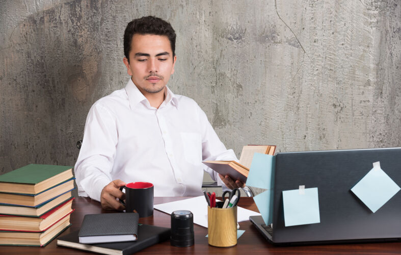 笔记本电脑年轻的商人在办公桌前看一杯茶拿着男性笔记本