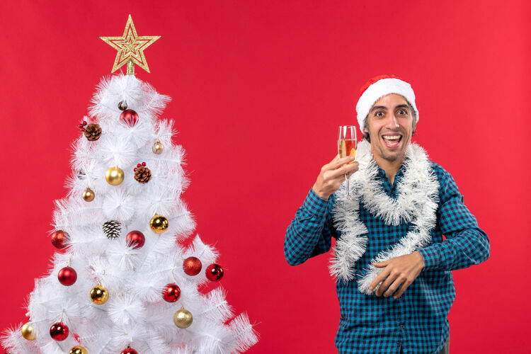庆祝戴着圣诞老人帽 举起一杯葡萄酒的疯狂年轻人在圣诞树旁为自己欢呼圣诞树帽子圣诞