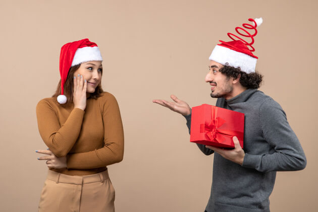 节日新年心情喜庆的概念与可爱的情侣戴着红色圣诞老人帽的女孩送他的礼物就灰色帽子帽子可爱