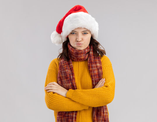站立被冒犯的年轻斯拉夫女孩戴着圣诞帽 脖子上围着围巾 双手交叉站在白色背景上 留着复制空间围巾女孩背景