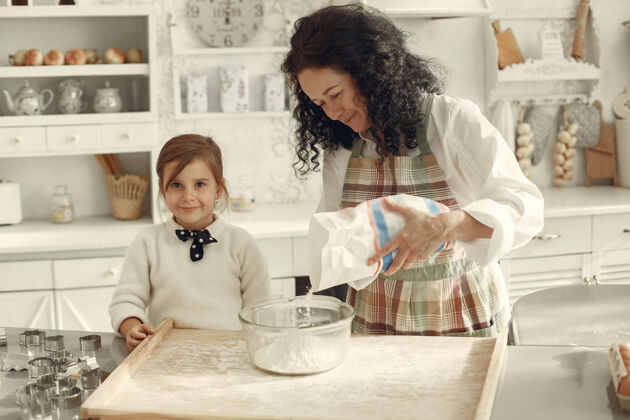 面包店厨房里的人奶奶带着小女儿成年妇女教小女孩做饭卷发黑发蛋糕