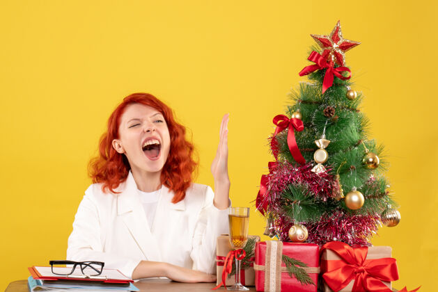 礼物正面图：女医生坐在桌子后面 手举着圣诞礼物 背景是黄色的情感手女医生