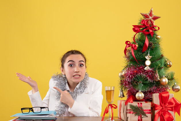 女正面图：女医生坐在黄色背景的桌子后面 还有圣诞树和礼品盒新郎护士女医生