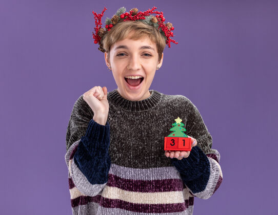 日期快乐的年轻漂亮女孩戴着圣诞花环拿着圣诞树玩具和日期做是的手势孤立在紫色的墙上头美丽穿