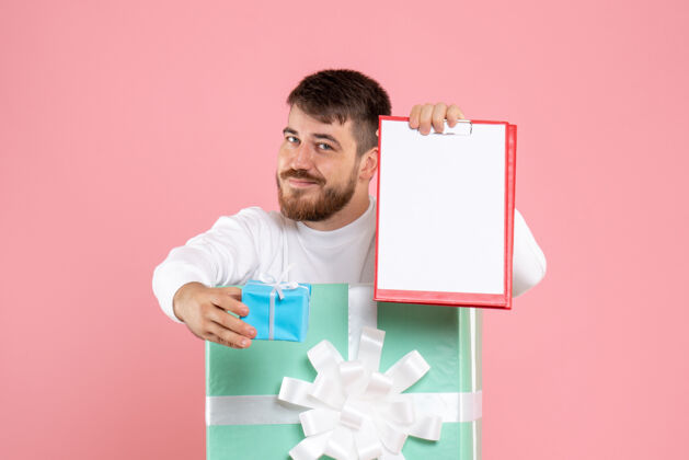 成人年轻人在礼物盒内的正面视图 粉红色的墙上放着文件纸条圣诞节便条前面