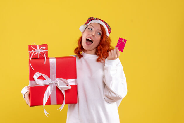 女人黄墙上年轻女子拿着圣诞礼物和银行卡的正面图微笑情感年轻的女人