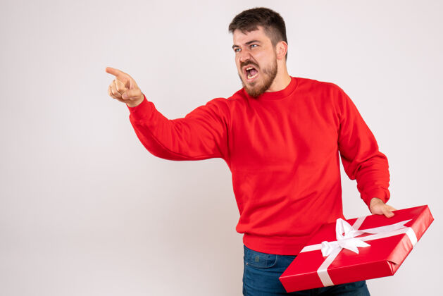 年轻身穿红衫的年轻人手持圣诞礼物 在白墙上与人争吵争论男性男人