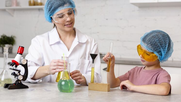创新者女老师和戴着发网的女孩用显微镜做科学实验安全眼镜导师实验