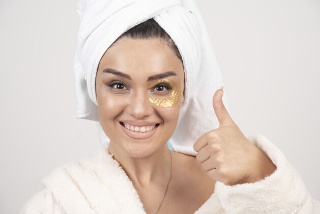快乐微笑的年轻黑发女子穿着浴衣与化妆品眼罩洁面乳水疗护肤