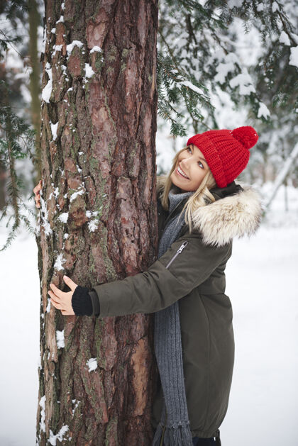 享受年轻的女人在冬天的森林里拥抱着树户外女人美丽