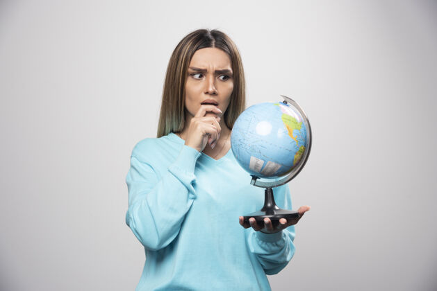 女性穿着蓝色运动衫的金发女孩手里拿着一个地球仪 仔细地思考 试图记住地理地球聪明