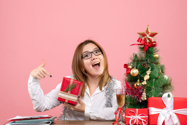 圣诞节女工正坐在粉红色的椅子上 手里拿着圣诞礼物电脑工作主任
