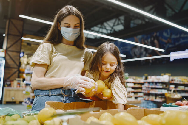 Covid19一家人在超市戴着防护面具的女人人们选择蔬菜母亲带着女儿冠状病毒女性面具货架