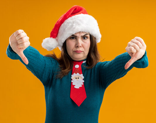 快乐未发布的成年白人妇女与圣诞帽和圣诞领带拇指向下孤立的橙色背景与复制空间背景圣诞节成人