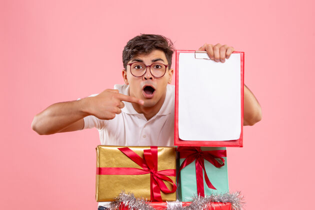 圣诞节年轻人圣诞节礼物的正面图 粉红色墙上拿着文件纸条礼物十二月礼物