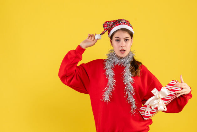 年轻正面图：穿着红色毛衣拿着礼物和圣诞帽的年轻女孩时尚服装圣诞老人