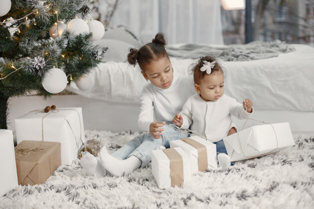 盒子穿着白色毛衣的孩子女儿们在圣诞树旁缝线两个姐妹在家毛衣家传统