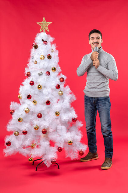 礼物新年气氛积极的家伙穿着牛仔裤站在装饰圣诞树附近圣诞树牛仔裤圣诞节