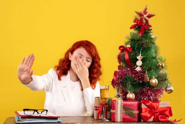 桌子女工人坐在桌子后面 手里拿着圣诞礼物和黄色的圣诞树女办公室圣诞节