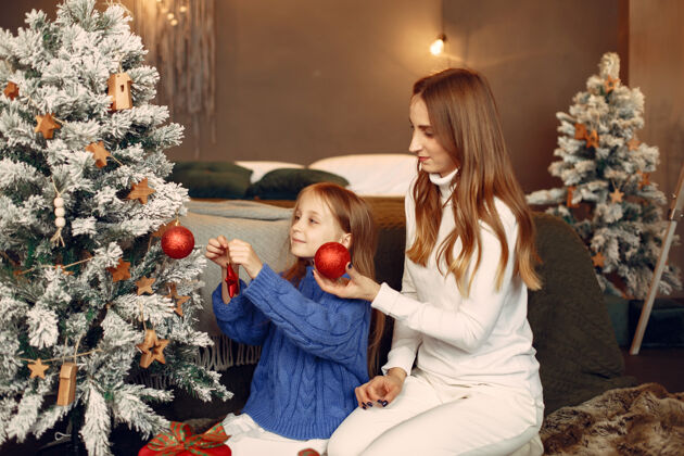 给人们在为圣诞节做准备母亲在和女儿玩耍一家人在节日的房间里休息孩子穿着蓝色毛衣人女孩节日