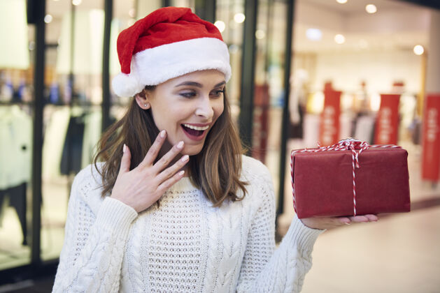 幽默兴奋的女人看着圣诞礼物享受零售圣诞装饰品